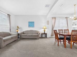Ein Wohnzimmer mit einer Couch, einem Esstisch mit Stühlen, einer Lampe und einem Gemälde an der Wand.