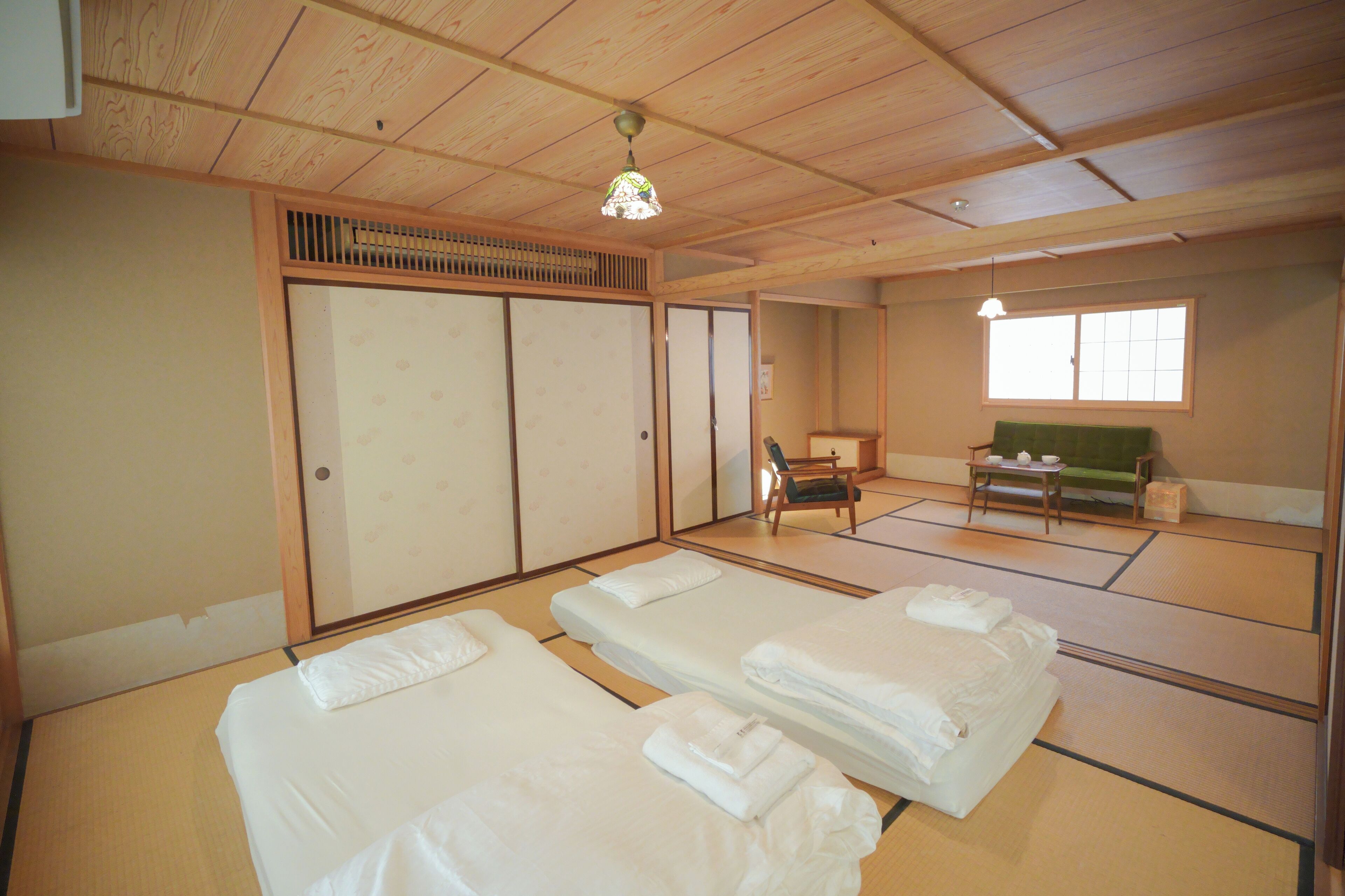 A traditional Japanese-style room with tatami flooring, two beds, a sliding door, a green sofa, and a small table with a teapot.