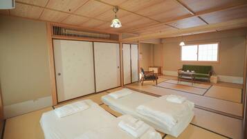 A traditional Japanese-style room with tatami flooring, two beds, a sliding door, a green sofa, and a small table with a teapot.