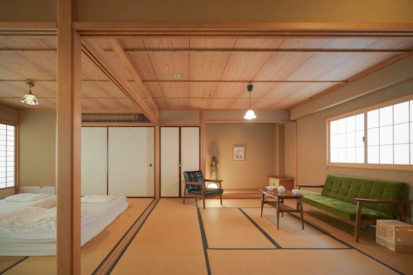 A traditional Japanese-style room with tatami flooring, a green sofa, a small table with a tea set, and a sliding door.