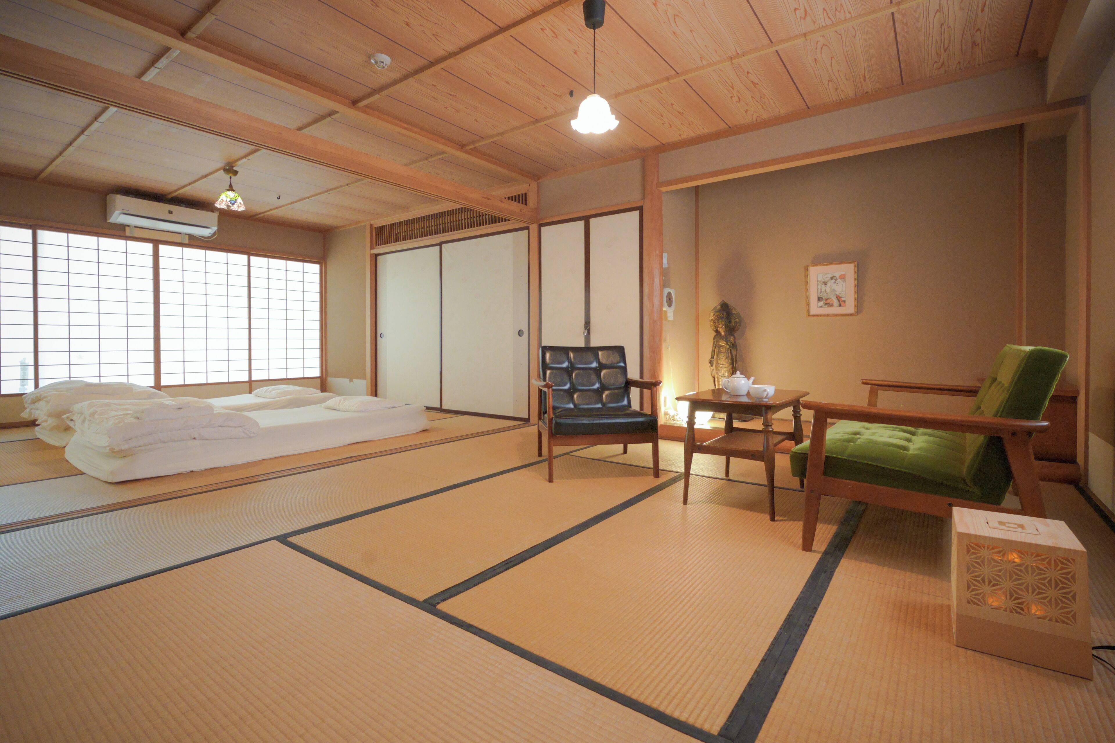 A traditional Japanese room with tatami flooring, a futon bed, a green chair, a wooden table, and sliding doors.