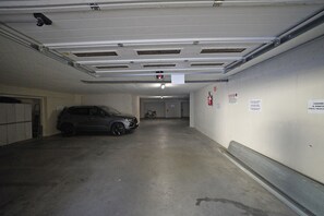 A parking garage with a car parked in a space, concrete walls, and a ceiling with ventilation. - Casa Matilda in Sirmione (Sirmione)