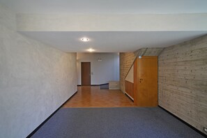 Un couloir avec une porte en bois, un interrupteur et un sol carrelé.