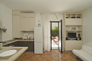 Une cuisine compacte équipée d’un réfrigérateur, d’un évier et de placards, donnant sur un balcon avec une table et des chaises.
