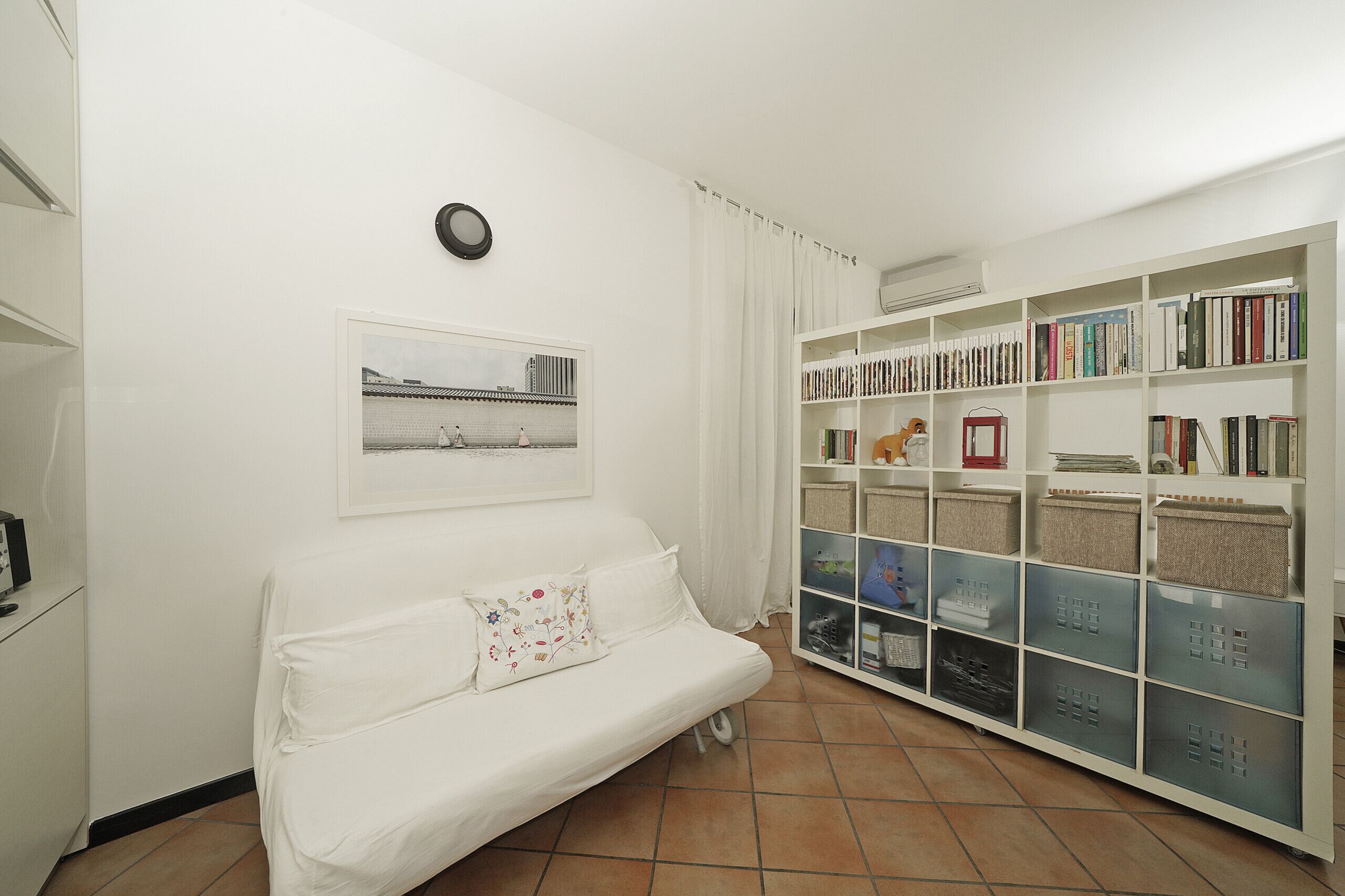 A room with a white sofa, a bookshelf, a framed picture, and a clock on the wall.