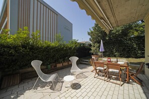 Une terrasse extérieure avec une table et des chaises, un pot de fleurs et un bâtiment sur lequel on peut lire l’inscription « HÔTEL EUROPA ».