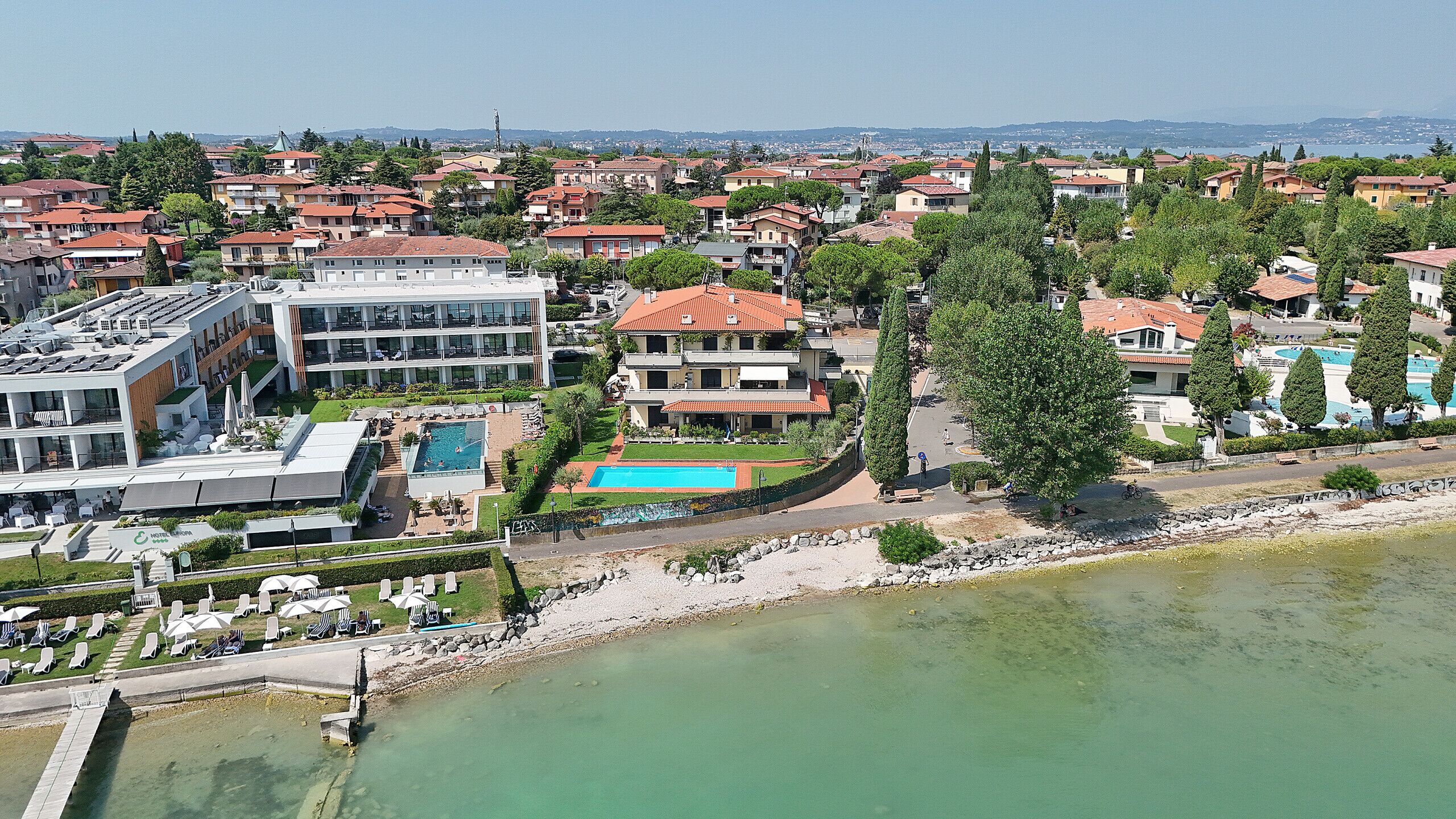 A coastal hotel with a swimming pool, multiple buildings, and a view of the sea.