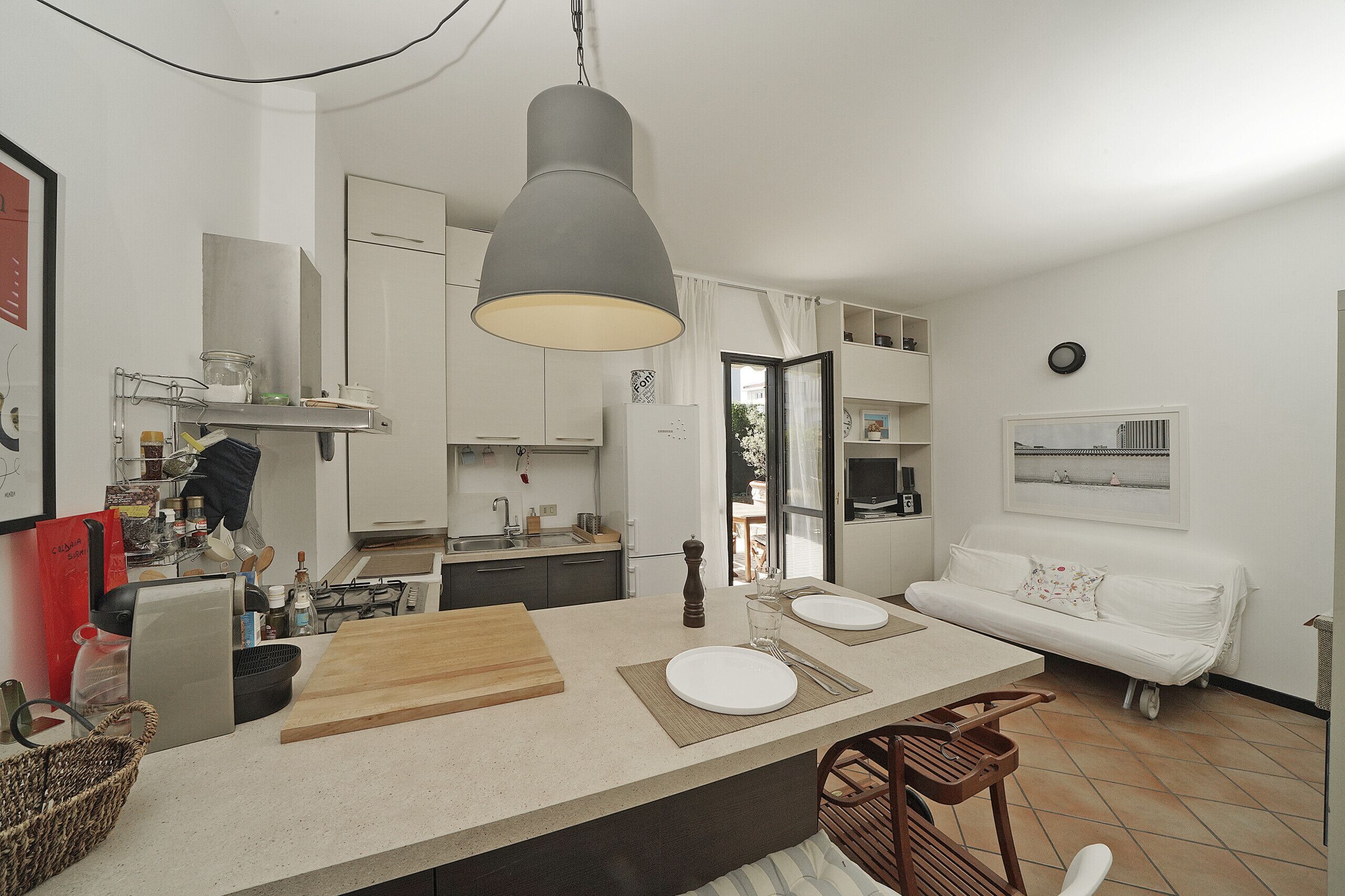 Una cocina moderna con una isla central, un área de comedor con sofá blanco y vistas a través de un ventanal.