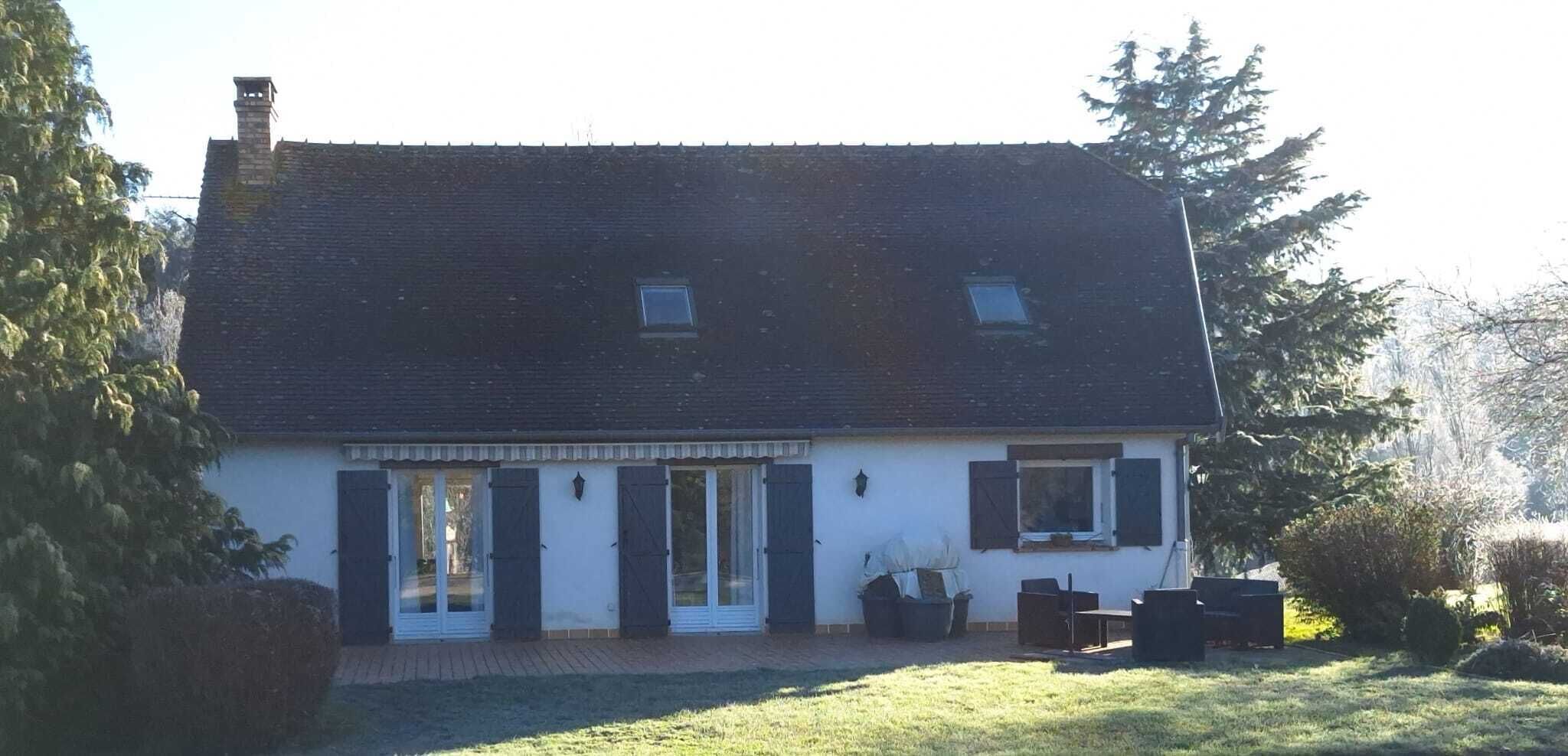 Une maison à deux étages avec une cheminée en briques, un porche à l’avant et un petit jardin.