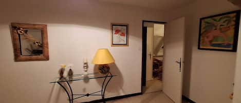 Ein Flur mit einem Glastischchen, einer Lampe, einem Spiegel und gerahmten Kunstwerken an den Wänden.