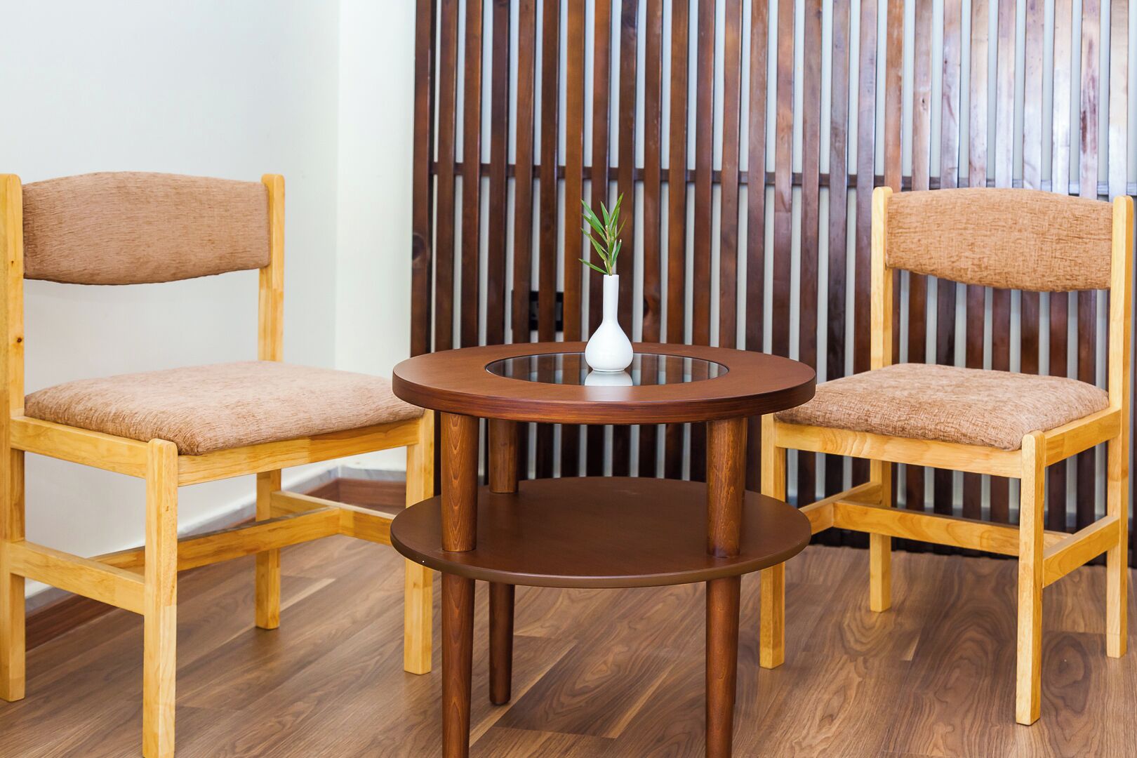 Duas cadeiras de madeira com assentos acolchoados e uma mesa redonda de madeira com um vaso branco no centro.