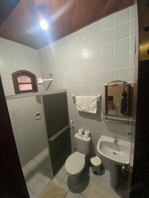 A compact bathroom with a toilet, sink, and a small window. - Pousada Caranà (Salinópolis)