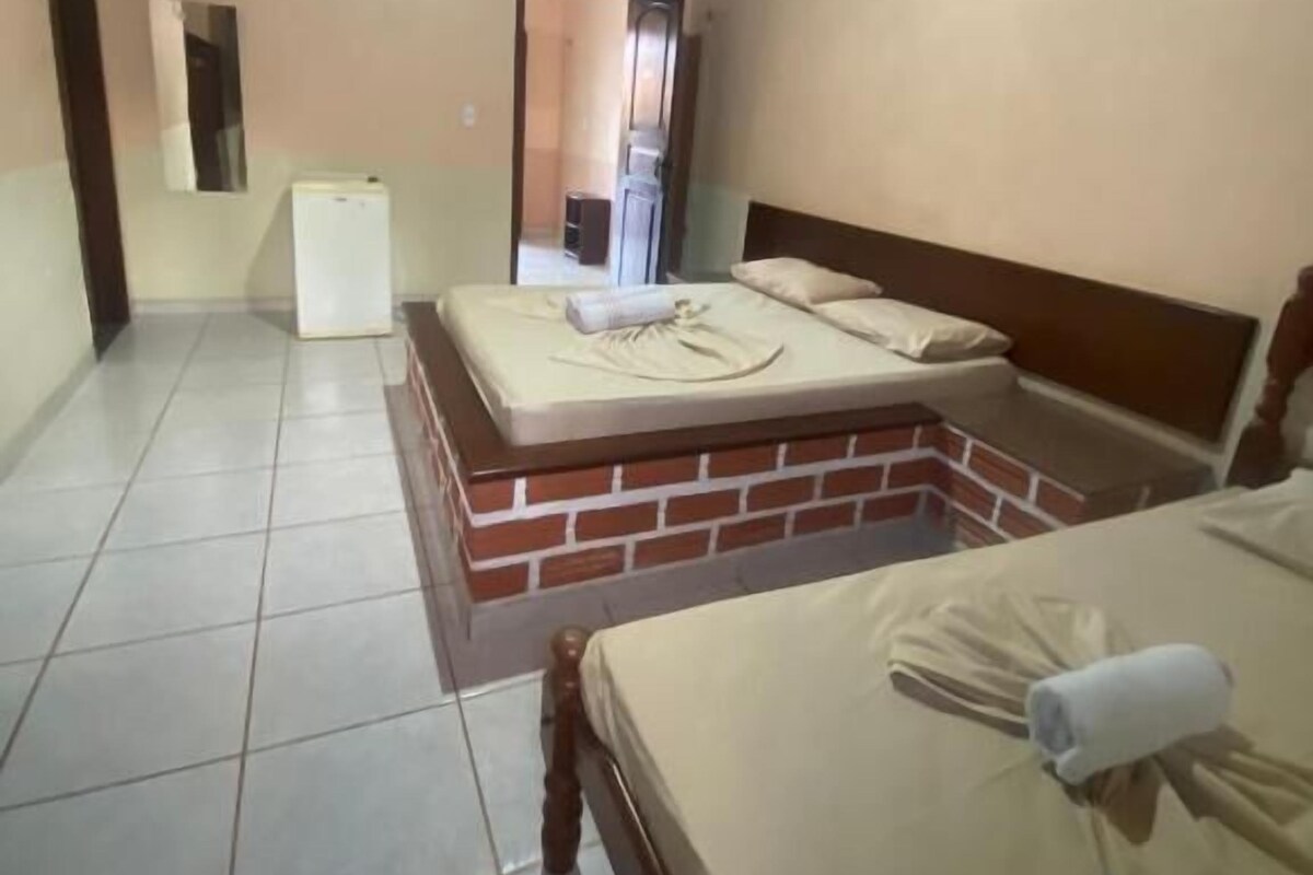 A room with two beds, a refrigerator, and a brick wall.
