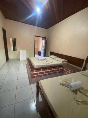 A room with two beds, a refrigerator, and a brick wall. - Pousada Caranà (Salinópolis)