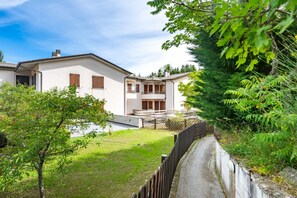 Ein Wohngebäude mit einem Balkon, einem umzäunten Garten und einem Weg zum Eingang.