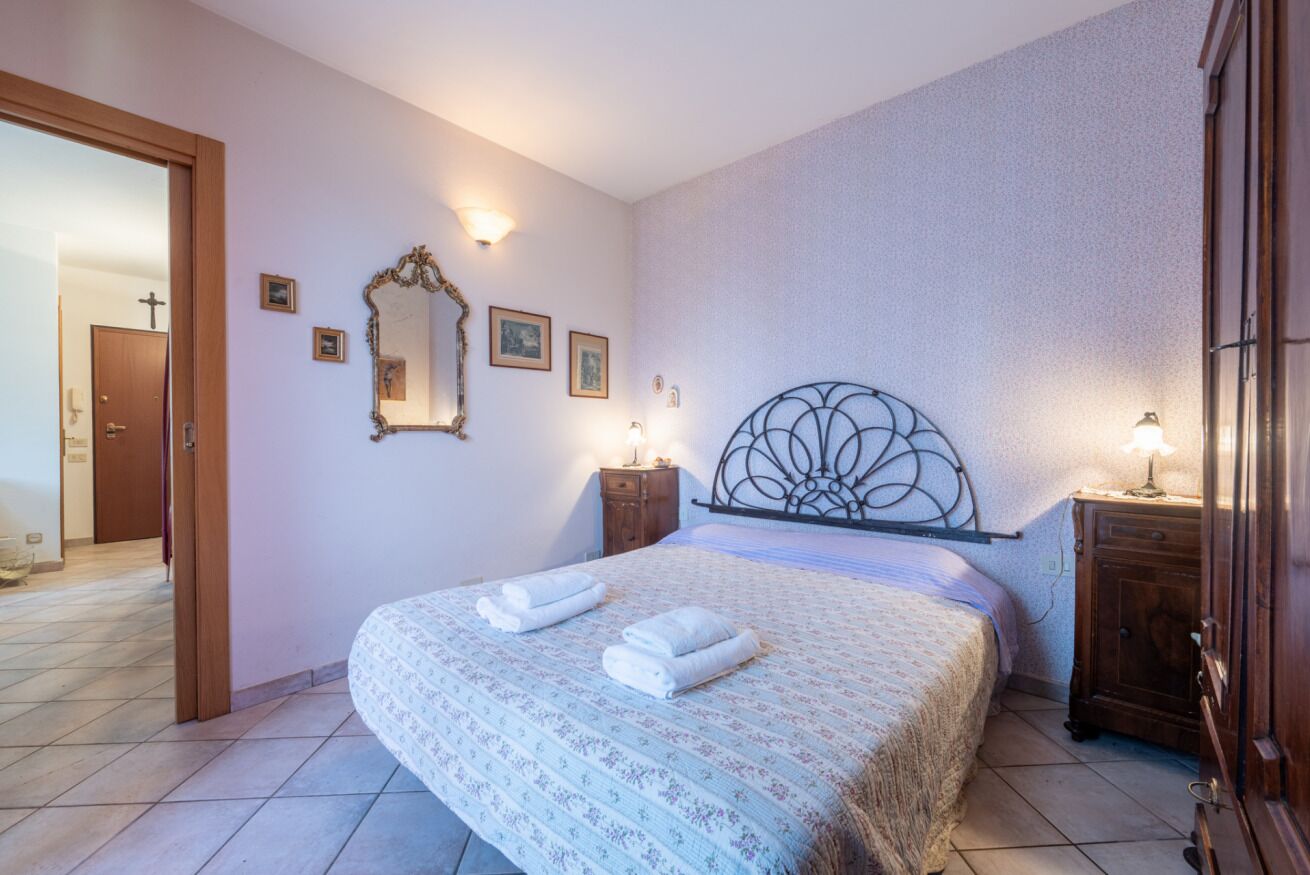 Ein Schlafzimmer mit einem großen Bett, zwei Nachttischen, einem Spiegel und einer Tür zu einem weiteren Zimmer.