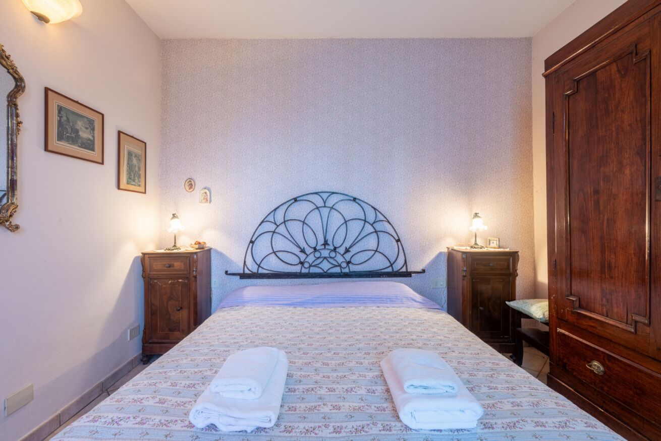 A hotel room with a bed, two bedside tables, a wooden wardrobe, and wall-mounted lamps.