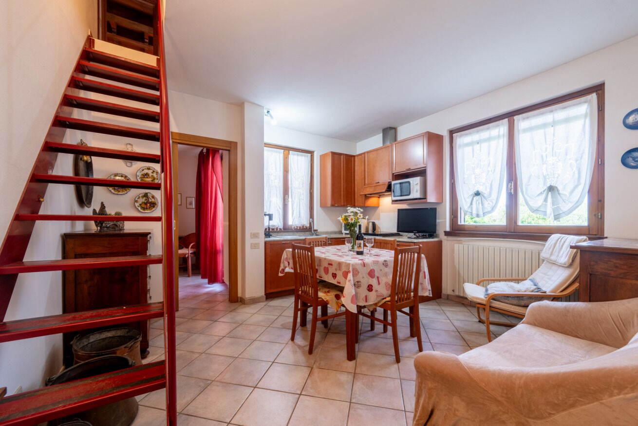 A kitchen with wooden cabinets, a dining table with chairs, a sofa, and a staircase.