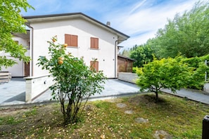 Ein zweigeschossiges Haus mit Garten, einer gepflasterten Auffahrt und einem kleinen Baum mit gelben Blüten.