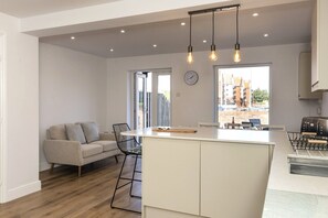 A modern kitchen with a central island, a dining area with a sofa and chairs, and a view of the outside. - Harbourside Haven - stylish marina living (Eastbourne)
