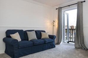 Ein Zimmer mit einem blauen Sofa, einer Stehlampe und Blick auf eine Marina durch ein mit Vorhängen versehenes Fenster.