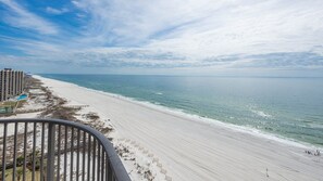 A beach with a clear sky, a sandy shore, and a building with balconies. - Phoenix Ix 1407 2 Bedroom Condo (Orange Beach)