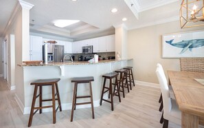 A kitchen with white cabinets, a granite countertop, and a central island with bar stools. - Phoenix Ix 1407 2 Bedroom Condo (Orange Beach)