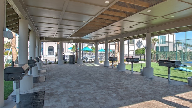 An outdoor covered patio area with grill stations, seating, and a view of the pool. - The Oasis 1509 Formerly Phoenix West Ii 1509 3 Bedroom Condo (Orange Beach)