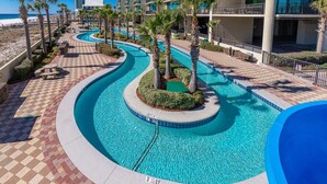 A pool area with a curved design, palm trees, and a view of a hotel building. - Phoenix West 307 3 Bedroom Condo (Orange Beach)