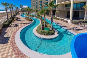 A pool area with a curved design, palm trees, and a view of a hotel building. - Phoenix West 307 3 Bedroom Condo (Orange Beach)