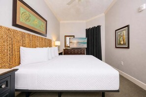 A hotel room with a large bed, a headboard with a woven design, a flat-screen TV, a dresser, and artwork on the walls. - Phoenix West 307 3 Bedroom Condo (Orange Beach)