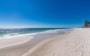 A beach with a clear sky, a sandy shore, and a building in the background. - Phoenix West 307 3 Bedroom Condo (Orange Beach)