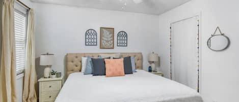 Un dormitorio con cama, mesitas de noche, ventilador de techo y decoración mural.