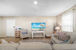 Ein Wohnzimmer mit Fernseher, einer Couch, einem Sessel und einem kleinen Tisch.
