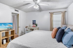 Een slaapkamer met een bed, een bureau, een stoel, een televisie en een plafondventilator.