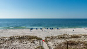Ein Strand mit Sonnenschirmen und Liegen, einer Flagge und dem Meer im Hintergrund.
