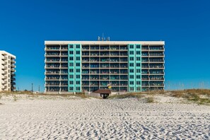 Ein mehrstöckiges Hotel mit einer zentralen Atriumlichtkuppel, Balkonen und einem Sandstrand im Vordergrund.