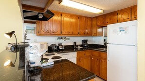 A kitchen with wooden cabinets, a black countertop, a white refrigerator, and a coffee maker. - Island Winds East 404 1 Bedroom Condo (Gulf Shores)