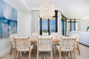 A dining area with a round table and six chairs, a chandelier, and a view of the outdoors. - The Oasis 1008 Formerly Phoenix West Ii 1008 3 Bedroom Condo (Orange Beach)