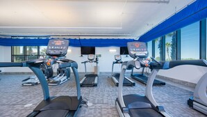 Un gimnasio con cintas de correr, bicicletas estáticas y una banca para pesas.