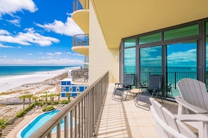 A balcony with a view of the beach, a pool, and lounge chairs. - Phoenix West 604 3 Bedroom Condo (Orange Beach)