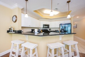 A kitchen with white cabinets, a black refrigerator, and a central island with bar stools. - Phoenix West 604 3 Bedroom Condo (Orange Beach)