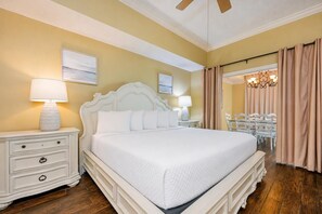 A hotel room with a large bed, two bedside tables with lamps, a ceiling fan, and a view of a dining area. - Phoenix West 604 3 Bedroom Condo (Orange Beach)