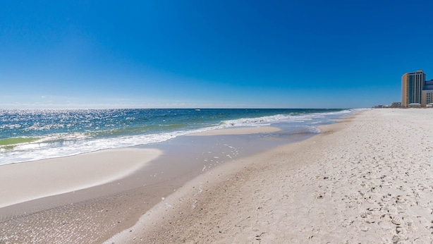 Una playa con cielo despejado, orilla arenosa y un edificio al fondo.