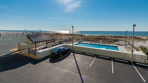 A parking lot with a pool area, a covered seating area, and a view of the beach. - Island Winds East 108 2 Bedroom Condo (Gulf Shores)
