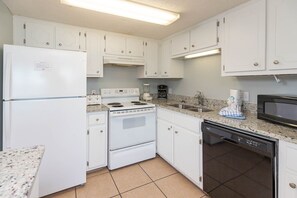 A compact kitchen with white cabinets, a built-in oven, a microwave, and a dishwasher. - Island Winds East 108 2 Bedroom Condo (Gulf Shores)