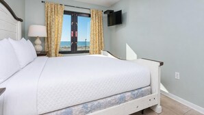 Una habitación de hotel con cama, televisión montada en la pared y ventana con cortinas.