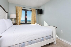 A hotel room with a bed, a TV mounted on the wall, and a window with curtains. - Island Winds East 108 2 Bedroom Condo (Gulf Shores)