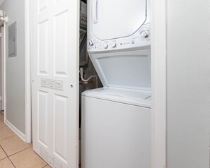 A laundry room with a front-loading washer and dryer, a door with a vent, and a tiled floor. - Island Winds East 108 2 Bedroom Condo (Gulf Shores)