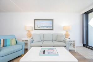 A living room with a light blue sofa, a white coffee table with a magazine, and two side tables with lamps. - Island Winds East 309 2 Bedroom Condo (Gulf Shores)